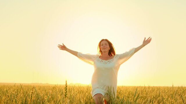 Beautiful carefree woman enjoying nature and sunlight in wheat field at incredible colorful sunset