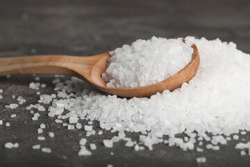 Natural sea salt and wooden spoon on grey table, closeup