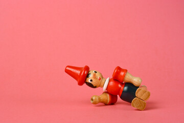Wooden puppet depicting Pinocchio fallng on a pink background