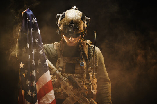 Special forces soldier holding US national flag in the dark