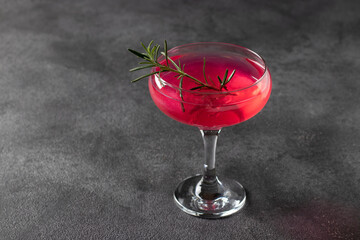 Sparkling rose wine with a shimmering edible sheen, garnished with rosemary on a dark background