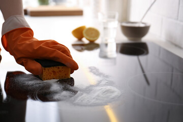 Woman using baking soda to clean electric cooktop indoors, closeup. Wrong detergent for such...