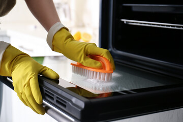 Woman cleaning oven door with baking soda in kitchen, closeup