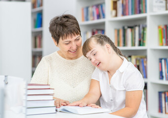 Fototapeta premium Teacher and girl with syndrome down read a book at library. Education for disabled children concept