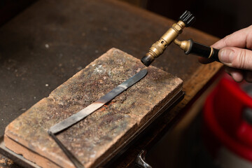 goldsmith jeweler heats a piece of silver with a gas torch to make a ring.