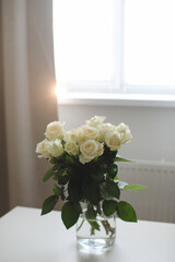  glass vase with white roses on white table indoors