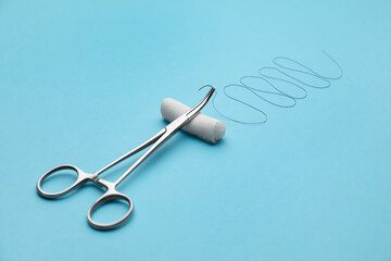 Forceps with suture thread and bandage roll on light blue background. Medical equipment