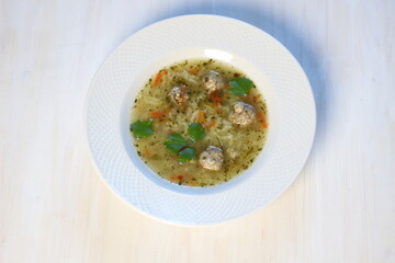 Soup with meatballs, rice, vegetables in white plate