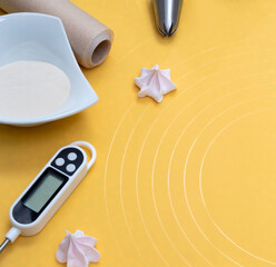 Meringue with a cooking tool, thermometer, flour, parchment. Yellow background with space for text. Selective focus.