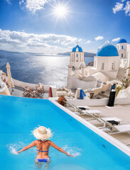 Santorini island with young woman in the swimming pool in Oia village against traditional churches, Greece