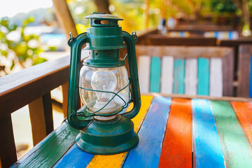 Green old fashioned lamp on colorful wooden table. Bright warm sun, vacation concept