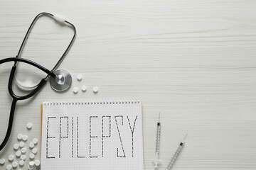 Notebook with word Epilepsy, stethoscope, pills and syringes on white wooden table, flat lay. Space for text