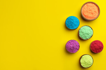 Colorful powders in bowls on yellow background, flat lay with space for text. Holi festival celebration
