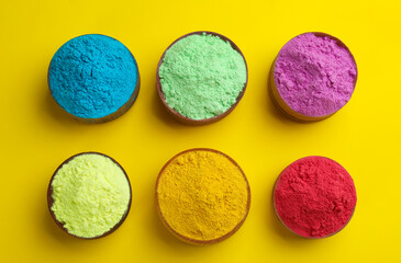 Colorful powders in bowls on yellow background, flat lay. Holi festival celebration