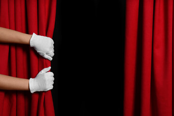 Woman opening red front curtains on black background, closeup. Space for text