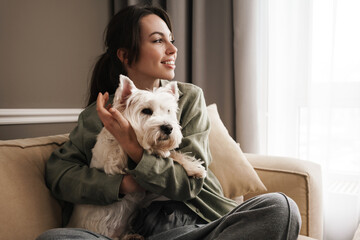 Happy white woman resting with her dog on sofa at home