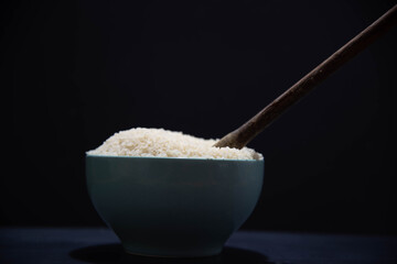 Porcelain pan with raw white rice and wooden spoon on black background.