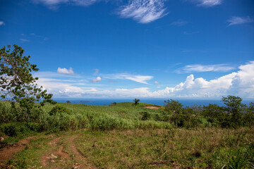 Green mountain and distant ocean under blue sky. Sunny rural landscape. Rural land scenery. Summer travel hiking in green hills. Untouched nature parkland. Volcanic island relief