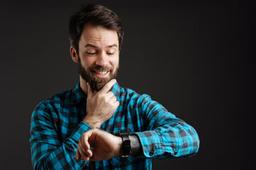 Bearded white happy man smiling while looking at his wristwatch