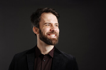 Bearded happy man in black jacket smiling and looking aside