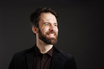 Fototapeta premium Bearded happy man in black jacket smiling and looking aside