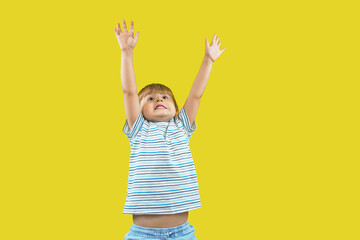 Toddler boy stretching and looking up, isolated on yellow background. Child raising hands and wants to grow. Mock up, copy space.