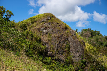 Fototapeta na wymiar Green mountain rock peak under blue sky optimistic landscape. Rural land scenery. Summer travel hiking in green hills. Untouched nature parkland. Volcanic island relief