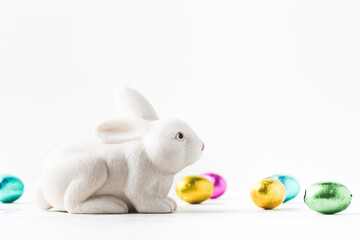 Macro shot of white rabbit among coloful eggs on the white background. Easter background