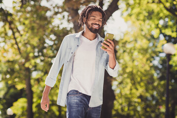 Portrait of attractive cheerful guy using device chatting strolling pastime fresh air outside...