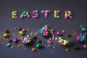 Chocolate Easter eggs full of candies, surrounded by colorful sweets on the grey background. Easter background. Easter sign made with candies