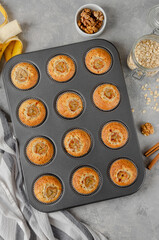 Banana muffins with oatmeal, walnuts and cinnamon in baking form on gray concrete background. Healthy dessert. Top view.