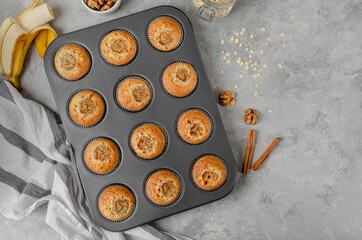 Banana muffins with oatmeal, walnuts and cinnamon in baking form on gray concrete background. Healthy dessert. Top view. Copy space.