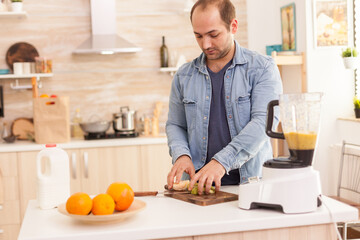 Guy prepares nutritious smoothie in kitchen with fresh fruits. Healthy carefree and cheerful lifestyle, eating diet and preparing breakfast in cozy sunny morning