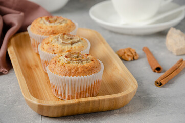 Banana muffins with oatmeal, walnuts and cinnamon on a wooden plate on gray concrete background. Healthy dessert.