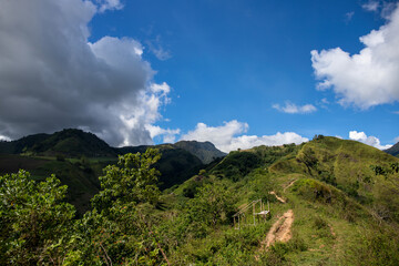 Green mountain range and walking path under blue sky landscape. Rural land scenery. Summer travel hiking in green hills. Untouched nature parkland. Volcanic island relief