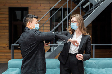 Male and female businesspeople concluding a business meeting are greeted by touching their elbows to each other, wearing protective medical masks