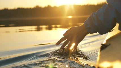 Fotobehang Slaapkamer man puts fingers down in lake kayaking against backdrop of golden sunset, unity harmony nature  © wifesun