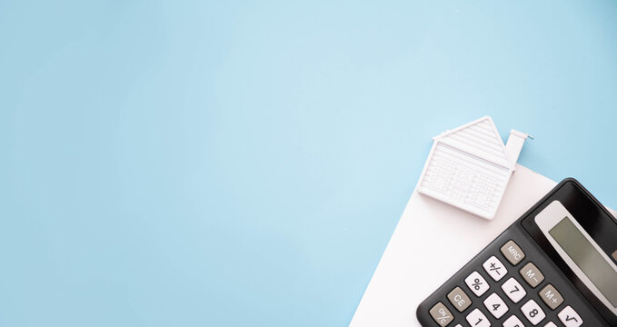 Top view of a miniature  house model, calculator and bills on blue background. Expense of home loan mortgage and home utility , economy and financial concept