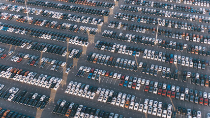 Huge parking with new cars in the territory of an automobile factory, aerial view. Overproduction of goods, economic crisis, no buyers.