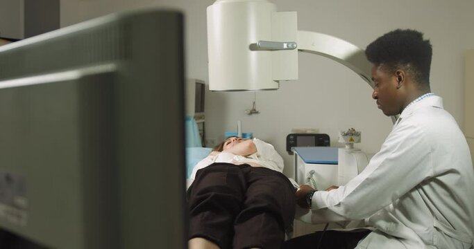 Extracorporeal shock wave therapy. Kidney stone treatment. Front view of African male doctor looking at the digital screen of the lithotriptor to determine stones position of woman patient