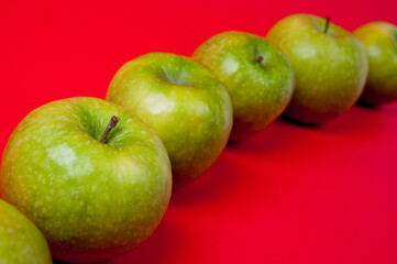 Large green apples, ripe and juicy. Photographed against a uniform red background.