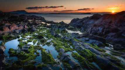 Sunset on a scenic rocky beach on the West coast of Scotland.Puddles of water and rocks with seaweed exposed at low tide.Beautiful coastal landscape scenery. © Jazzlove