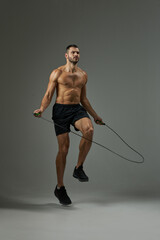 Adorable athlete with powerful body in shorts using skipping rope on the practice isolated on grey background © Friends Stock