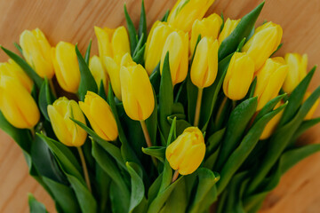 Obraz premium Bright fresh yellow tulips on wooden background. Many yellow tulips on wooden table. Bunch of flowers on the table.