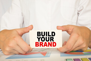 a man in the office holds a card with text BUILD YOUR BRAND . business concept