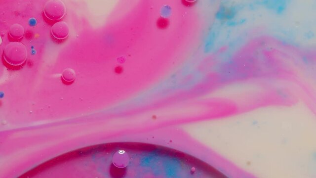 Top view movement of bright oil bubbles in slow motion. Multicolored surface background. Fantastic universe structure of colorful moving pink bubbles. Artistic image of ink drops floating on water