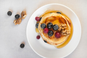 Flat lay of freshly cooked delicious pancakes with honey, walnut, raspberries and blueberries for breakfast.