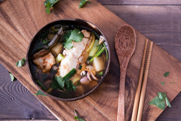 Asian soup with halibut and seafood (hemultan) shrimps, mussels and young octopus. Korean traditional soup on a dark wooden background with herbs. Wooden plate and spoon.