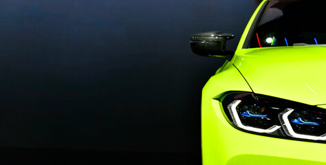 Front headlights of green modern sport car on black background, free space on left side for text.	