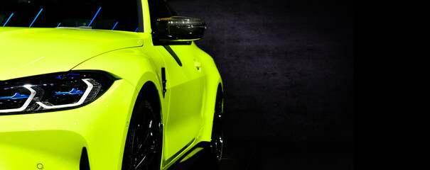 Front headlights of green modern sport car on black background, free space on right side for text.	
